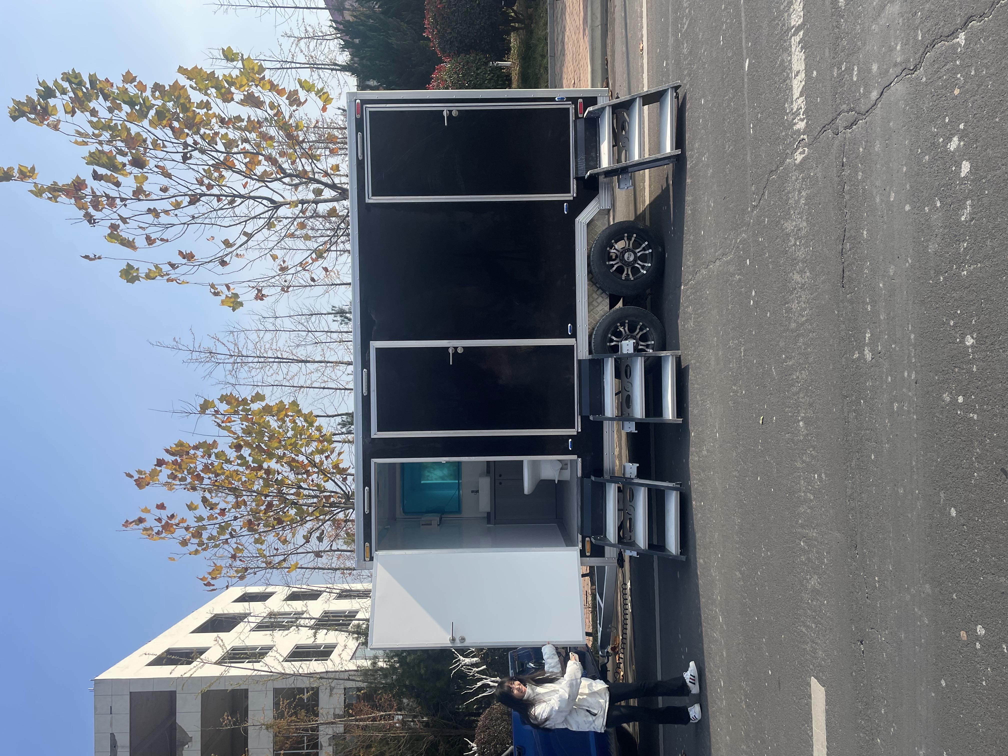 The black-clad mobile toilet trailer features a stepped boarding design