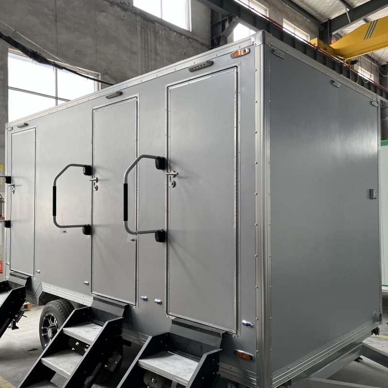 The grey trailer-mounted mobile toilet with multiple doors and handrails is a practical outdoor choice